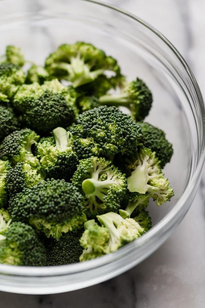 broccoli florets in a clear glass bowl atop a marble counter