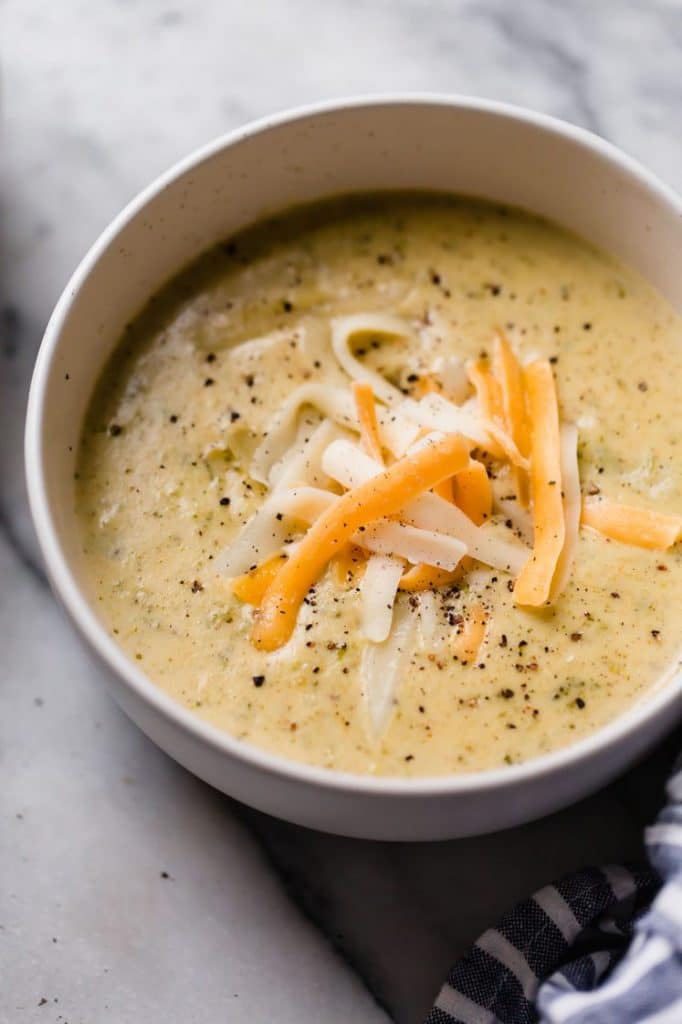 a bowl of instant pot broccoli cheese soup on top of a marble kitchen counter