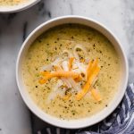 two bowls of instant pot brococli cheese soup atop a marble kitchen counter