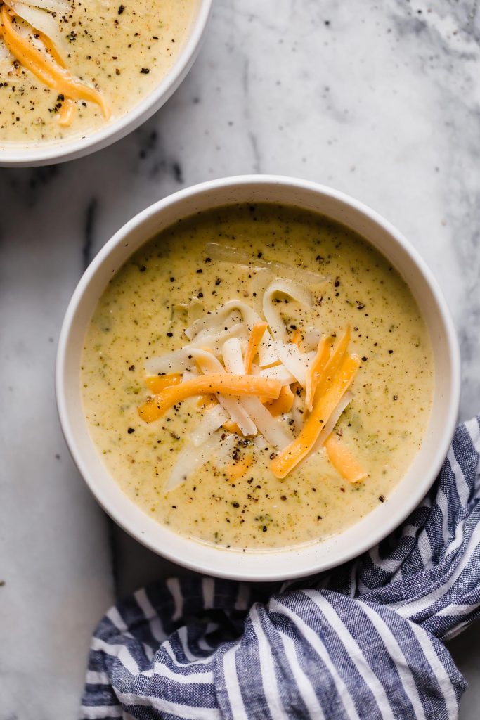 two bowls of instant pot brococli cheese soup atop a marble kitchen counter