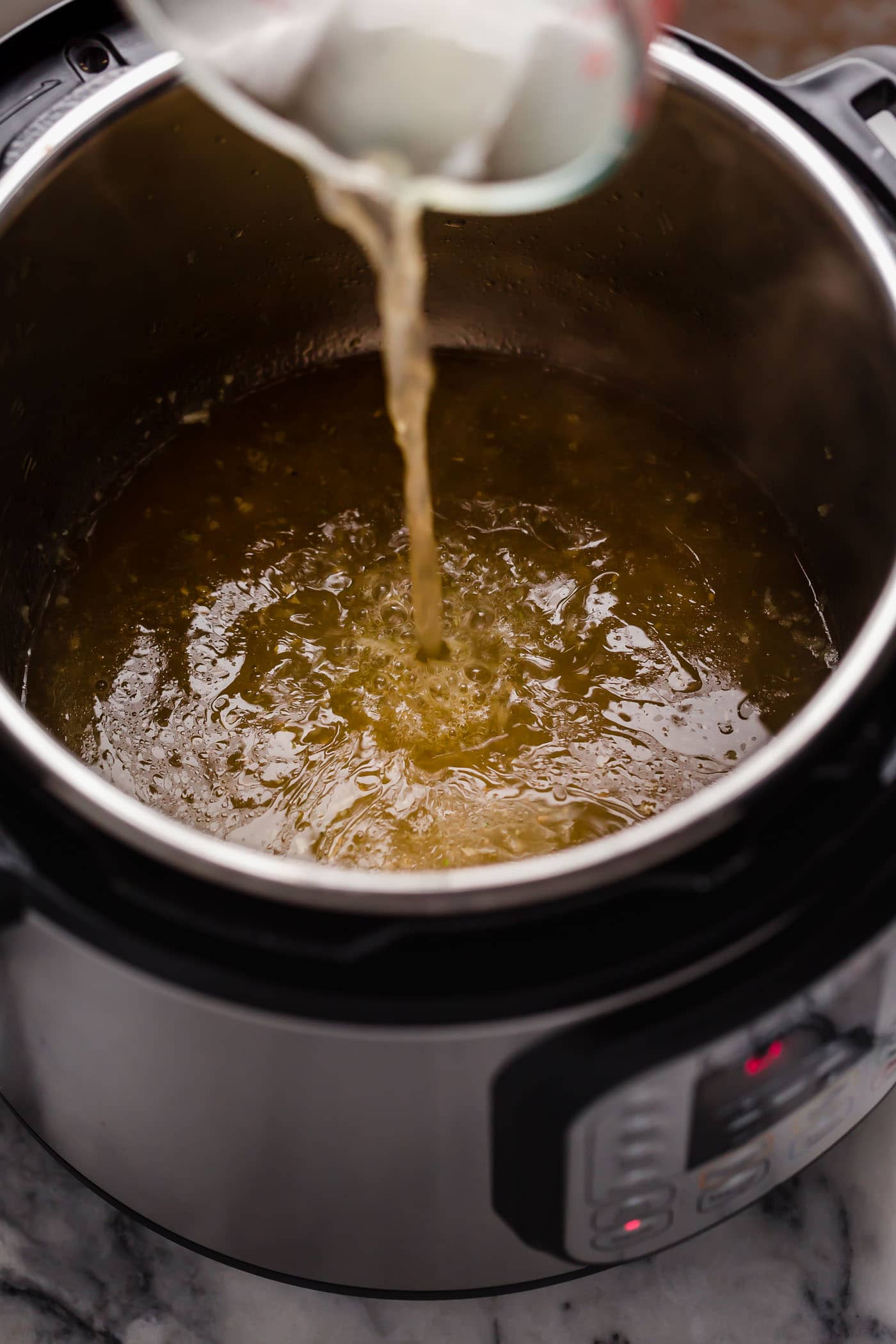 broth poured into instant pot with sauteed garlic in butter
