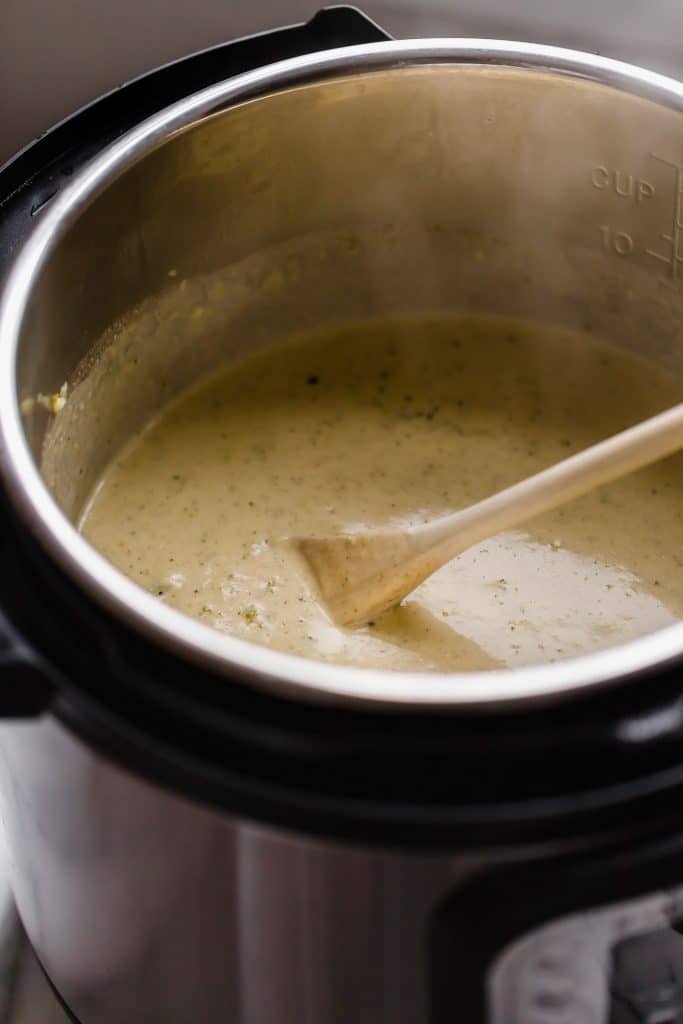 instant pot half full with broccoli cheese soup stirred with a wooden spoon