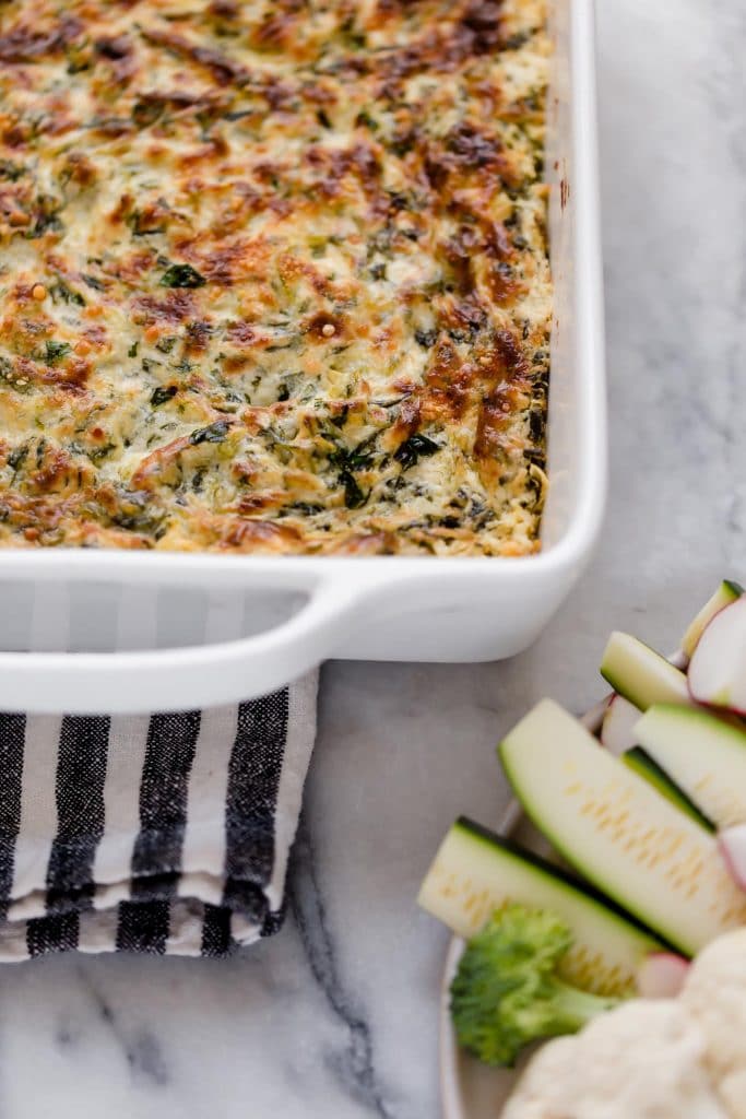 jalapeno spinach artichoke dip in a baking dish beside a bowl of low carb veggies