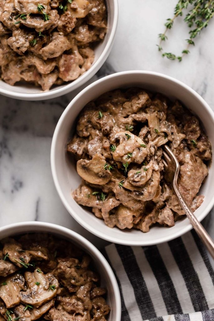 close up shot of three bowls of keto beef stroganoff atop a marble kitchen counter
