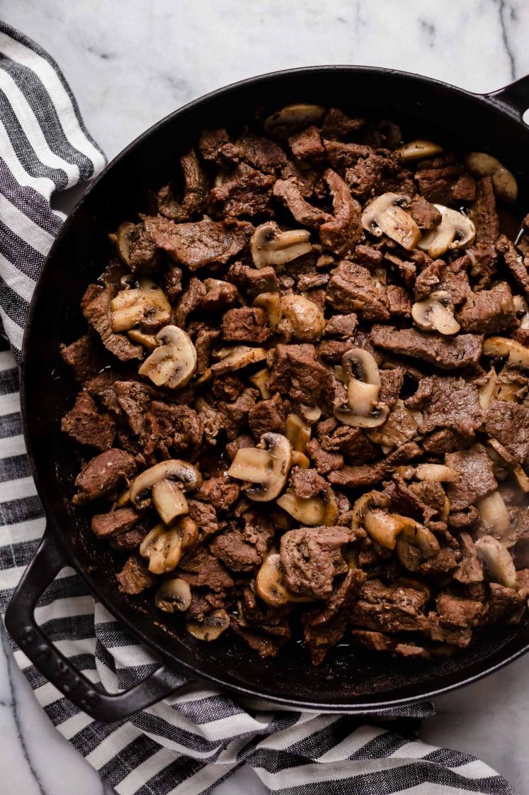 chopped seasoned and cooked beef stirred in with sliced button mushrooms in a large cast iron sauce pan