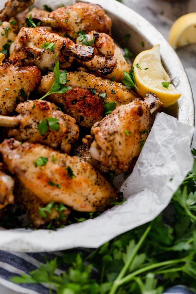 lemon pepper chicken wings in a bowl with lemon wedges and parsley