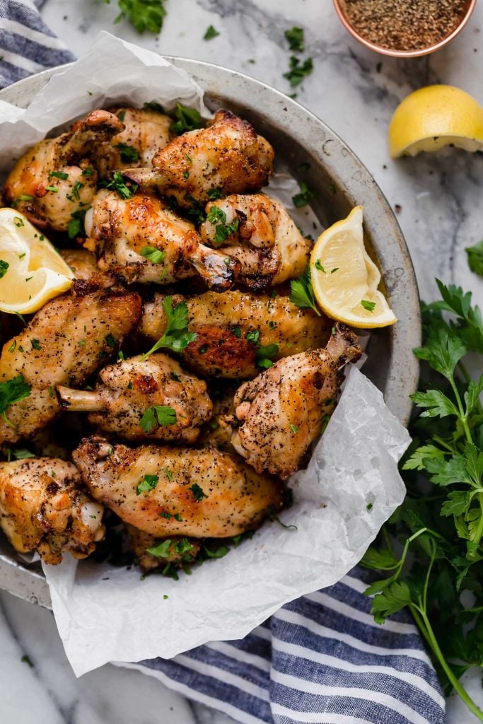 hero shot lemon pepper chicken wings in a platter beside half a lemon and parsley