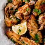 close up overhead shot of lemon pepper chicken wings with lemon wedge in a silver bowl