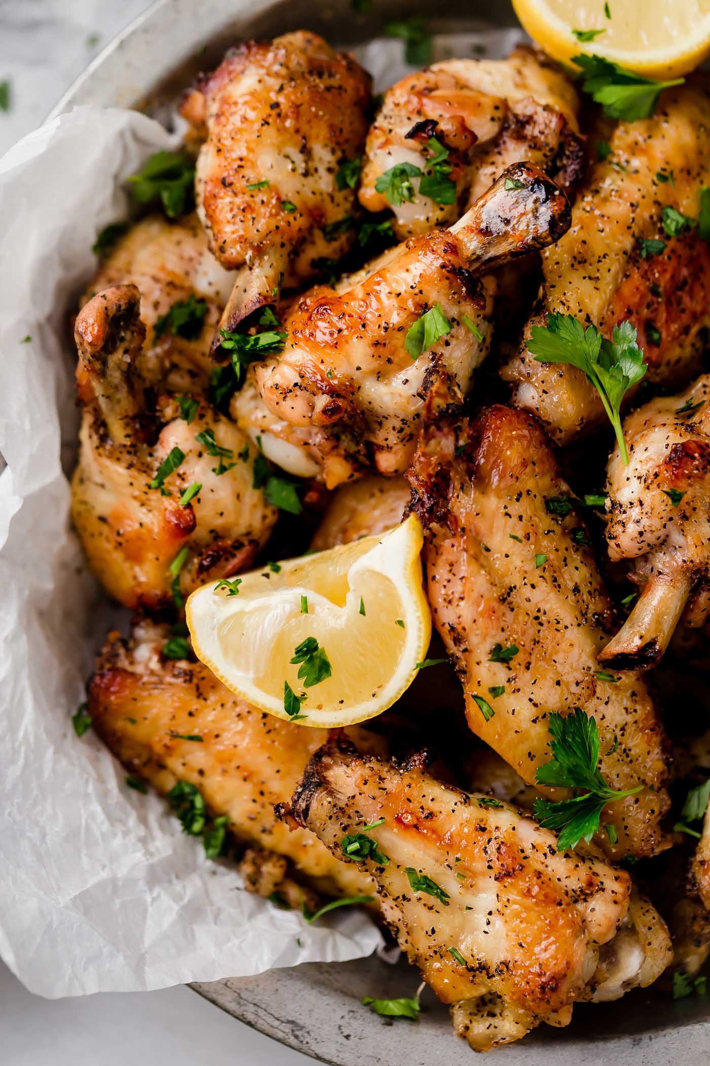 close up overhead shot of lemon pepper chicken wings with lemon wedge in a silver bowl