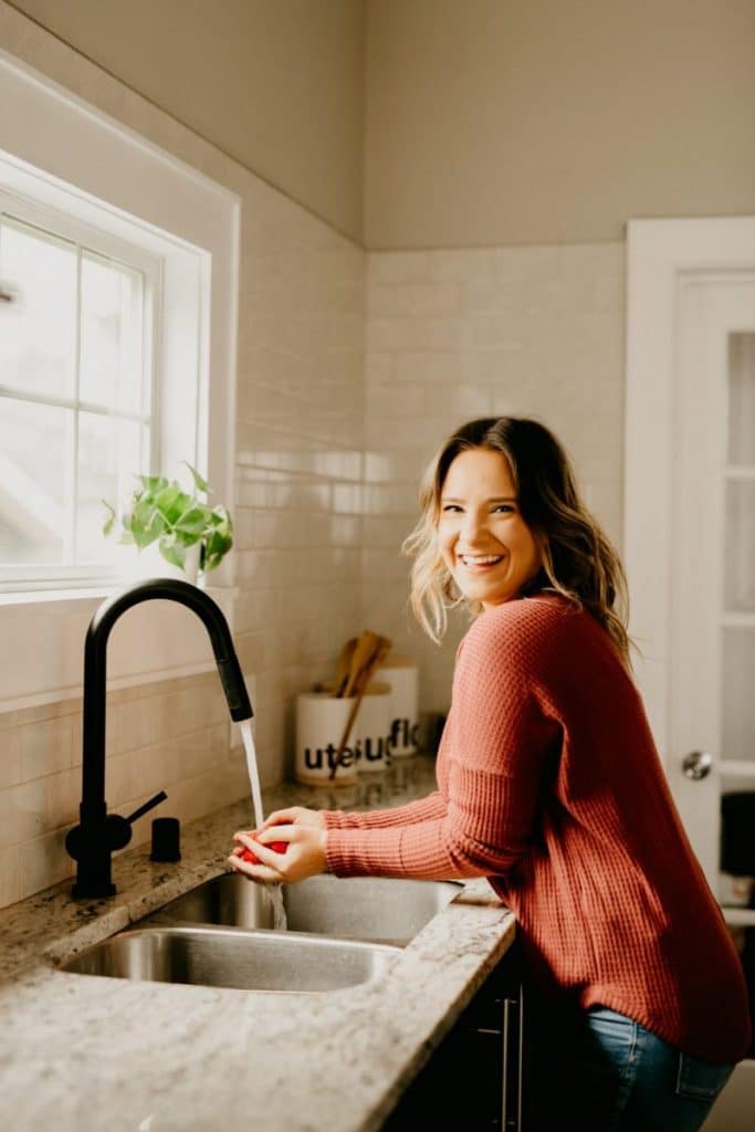 Sara smiling as she washes fruits on the kitchen sink