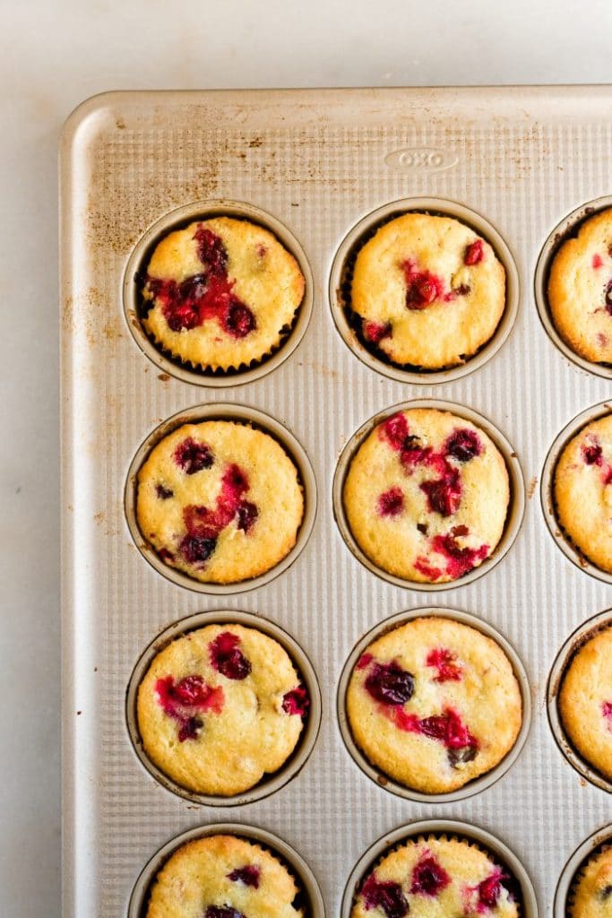 baked keto cranberry orange muffins in stainless steel muffin tin atop white countertop