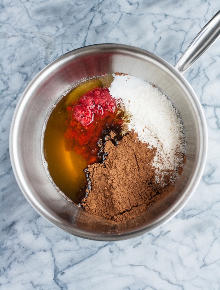 mashed raspberries, melted cocoa butter, cocoa powder, shredded coconut, monk fruit sweetener, and vanilla extract poured into stainless steel saucepan