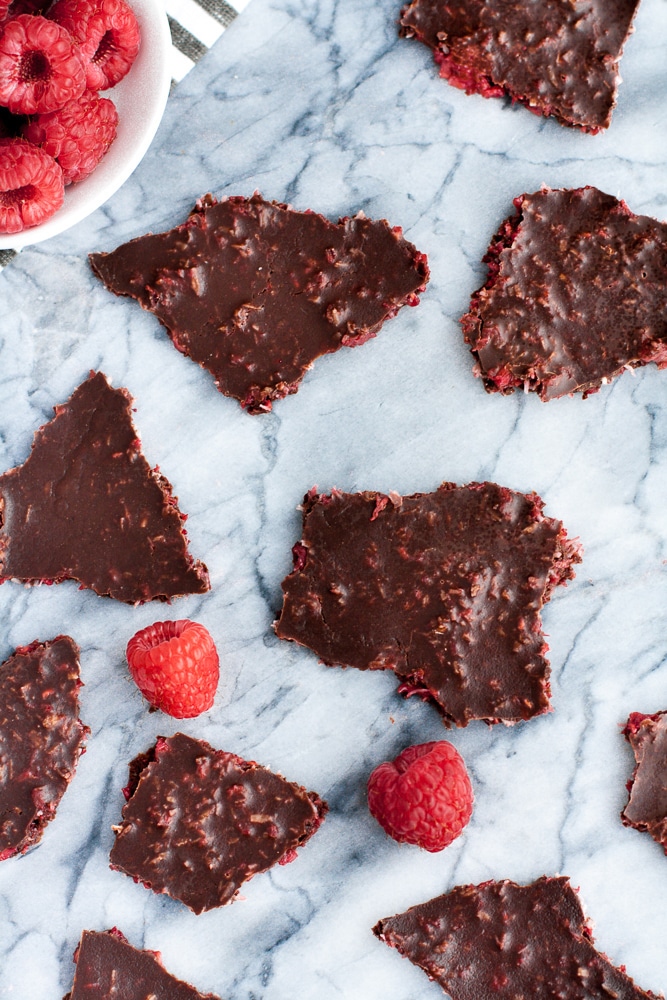 close up shot dark chocolate raspberry bark pieces atop a marble counter with fresh raspberries