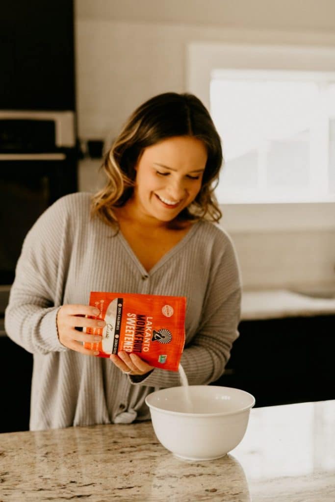 sara nelson pouring classic monk fruit sweetener into a white ceramic bowl atop a marble kitchen counter