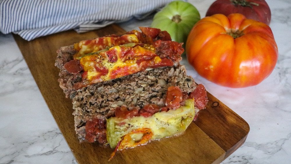 The Best Keto MEatloaf on a cheeseboard beside fresh whole tomatoes