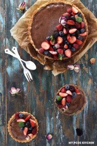 Low Carb No Bake Chocolate Tart with Raspberries on top of a wooden surface with two smaller tarts