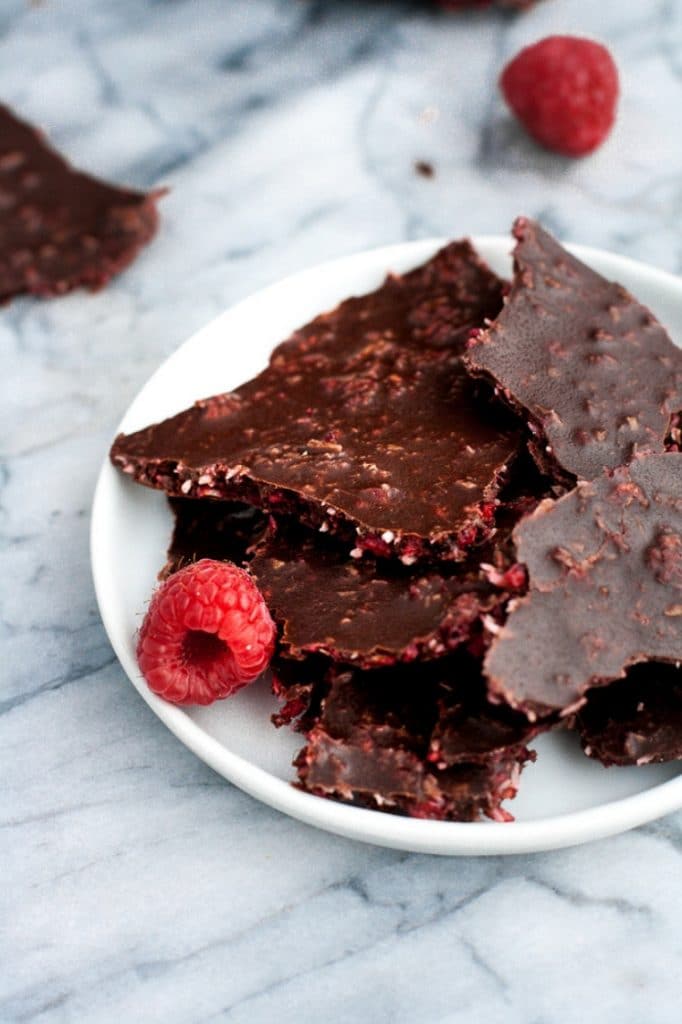 dark chocolate raspberry bark with a fresh raspberry on a small white plate