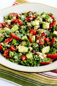 tomato salad with avocado, tuna, cilantro, and lime on a plate atop a striped table napkin