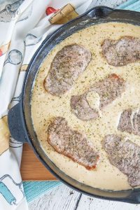 low-carb pork chops in creamy parmesan sauce in a cast iron skillet with baking pattern cloth aside