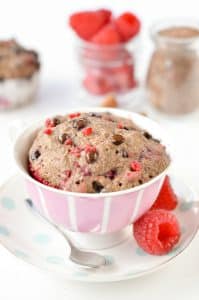 flaxseed muffin in a mug beside 2 raspberries and a teaspoon