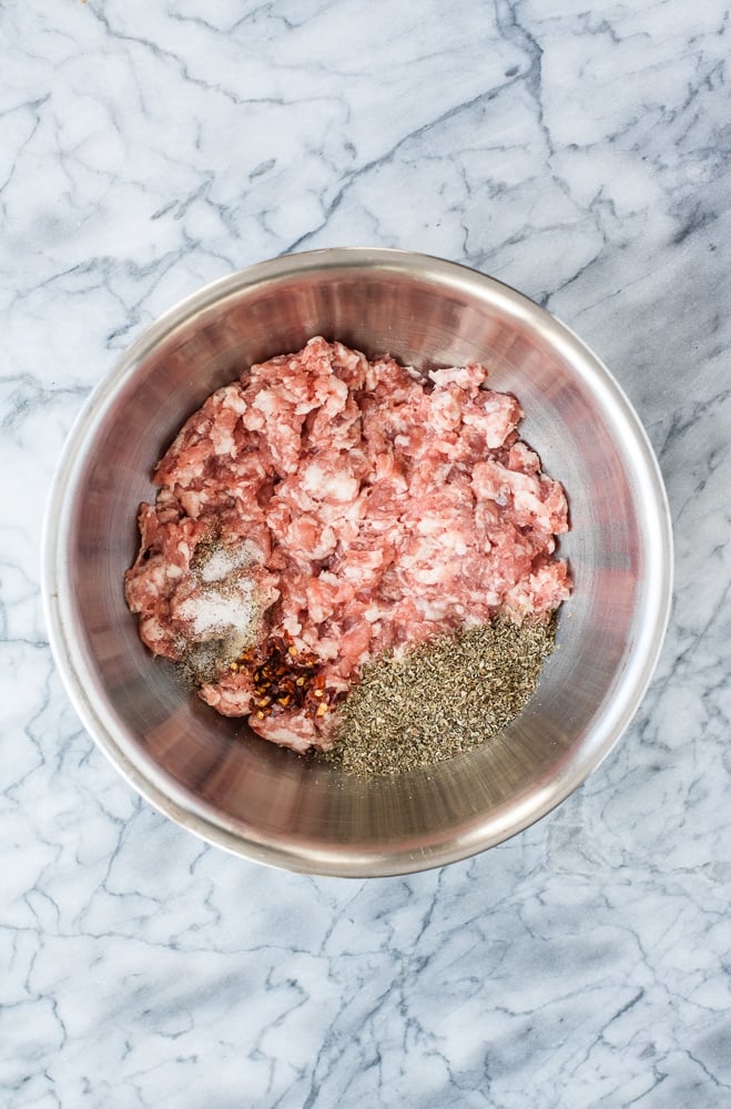 stainless steel mixing bowl with ground pork dried herbs and spices