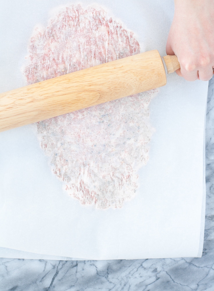 ground pork mixture in between two sheets of parchment paper rolled flat with a rolling pin