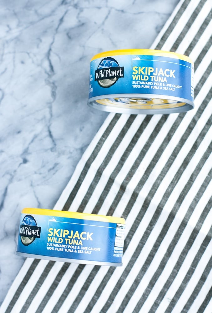 2 cans of Wild Planet Skipjack Wild Tuna atop a marble counter and cloth table napkin