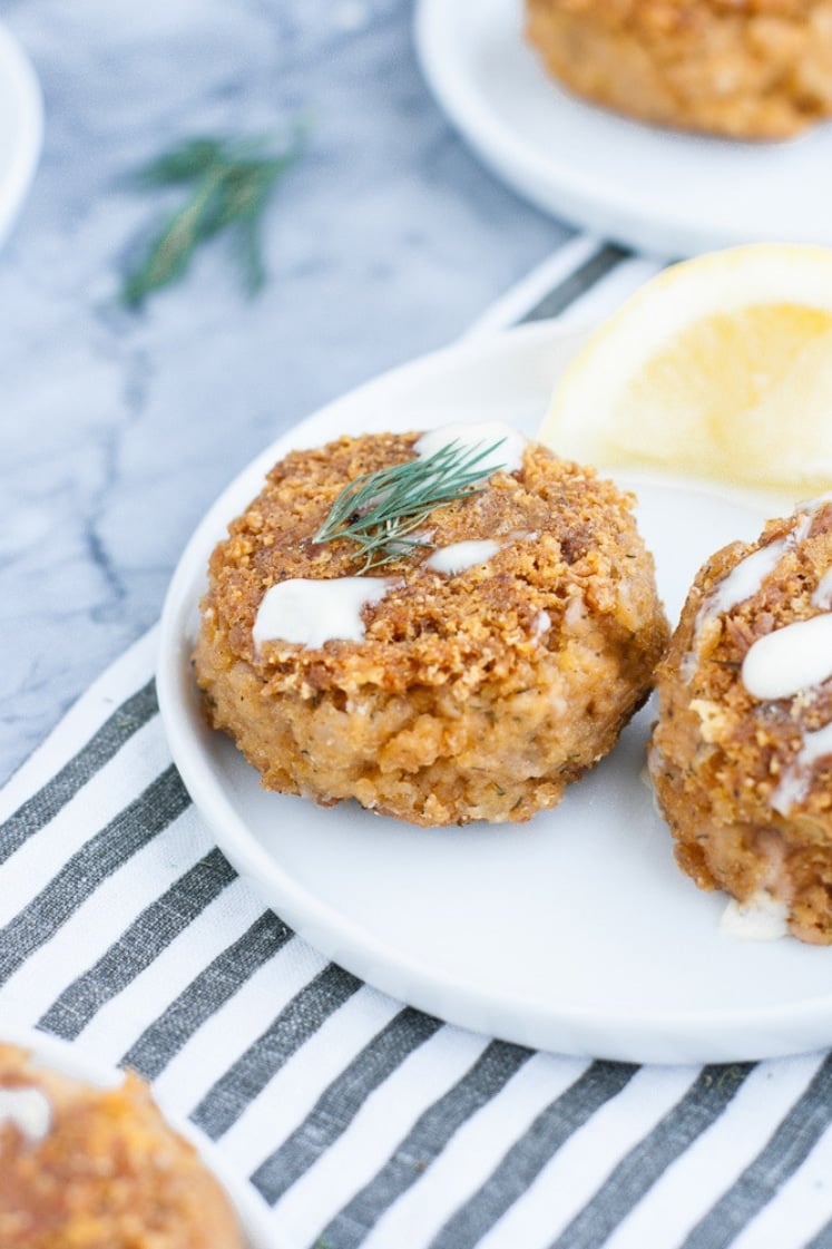 close up shot of 2 low carb tuna cakes on a white plate beside a wedge of lemon