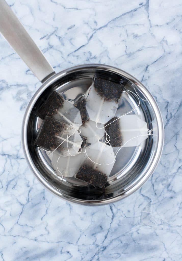 tea bags steeping in hot water on a stainless steel mixing bowl