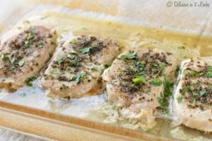 Tender butter and herb baked pork chops in a glass dish and topped with parsley