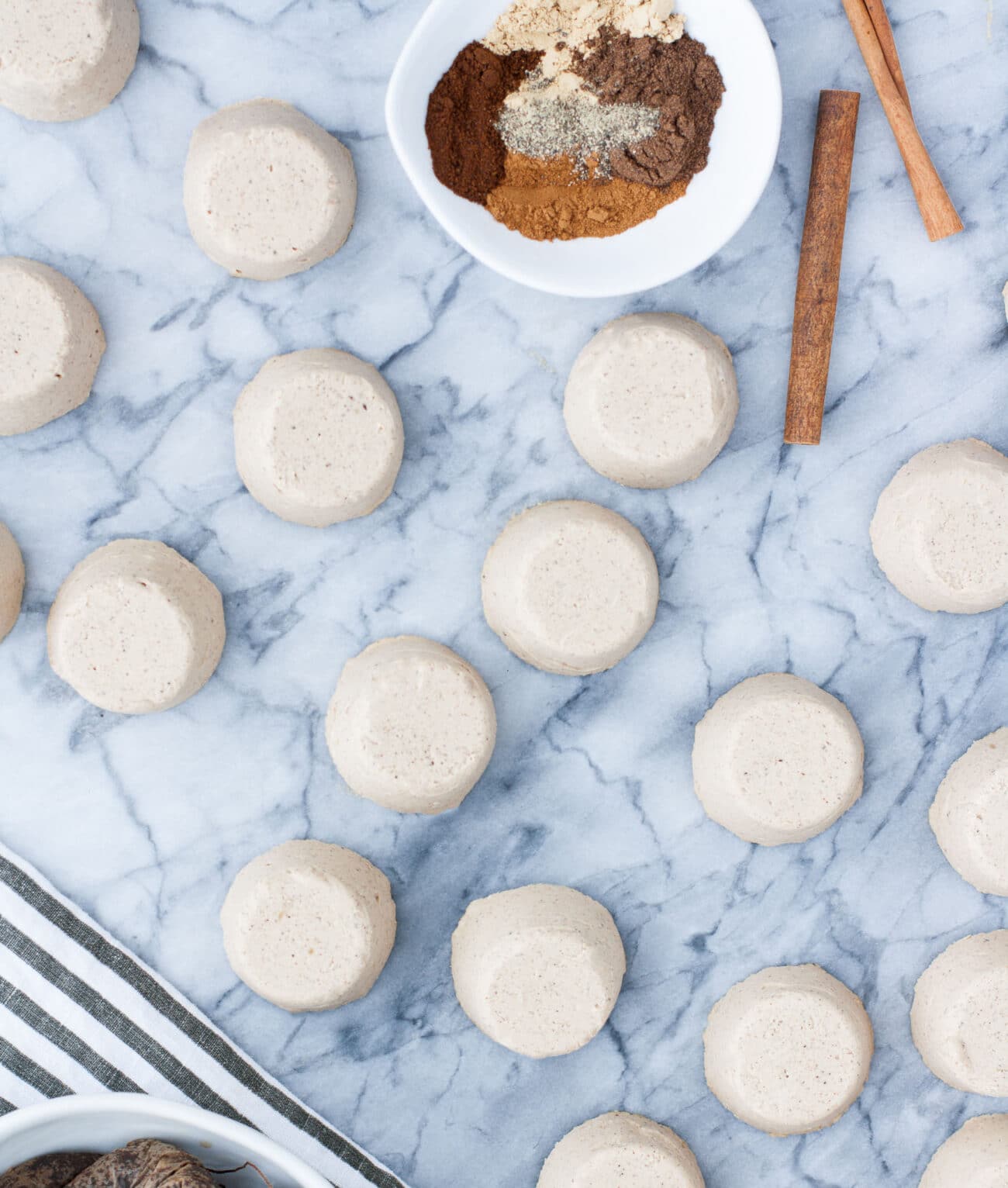 overhead shot of chai latte fat bombs on a marble kitchen counter beside a bowl of dry ingredients and 2 cinnamon sticks