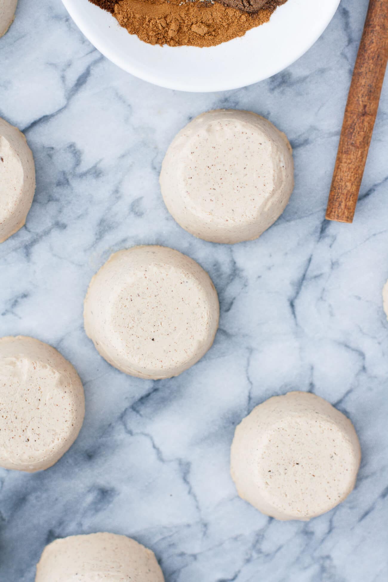 Chai Latte Fat Bombs on a marble counter beside a bowl of ingredients and a stick of cinnamon