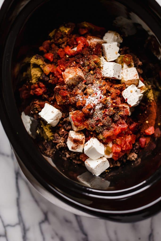 browned ground beef, cubed cream cheese, canned tomatoes with green chiles, chili powder, cumin, paprika, pepper, salt, and red pepper flakes in a slow cooker