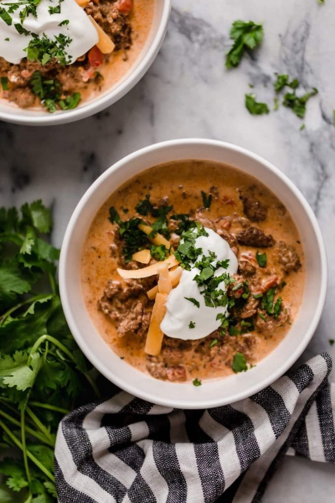 slow cooker taco soup in 1 serving bowls atop a marble counter beside sprigs of fresh parsley and a striped table napkin