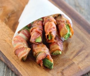 bacon wrapped avocado fries in parchment paper atop a wooden cheeseboard