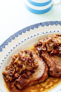 caramelized onion and bacon smothered pork chops on a blue and white vintage plate