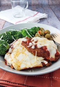 simple chicken parmesan on a dinner plate with broccoli and green olives