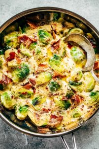 creamy cauliflower bacon garlic brussels sprouts in a sauce pan with a serving spoon