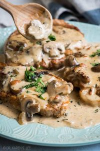 Wooden spoon pouring mushroom sauce on smothered pork chops on a light teal plate