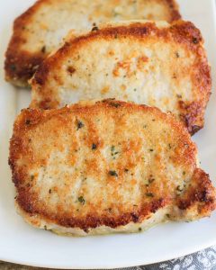 3 parmesan crusted pork chops laid on a white plate