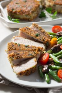 1 serving of easy parmesan crusted pork chopsserved on a white plate with green beans and cherry tomatoes