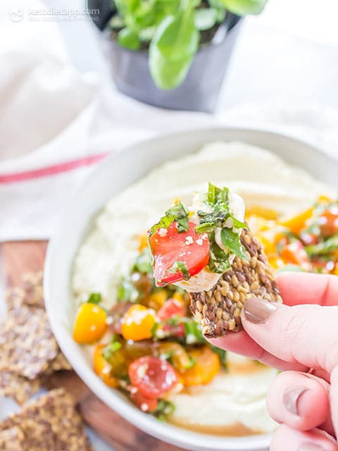 flax seed cracker being dipped into bruschetta feta dip