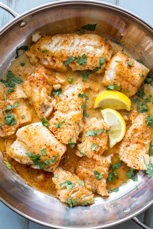 buttered cod in a skillet with lemon wedges and parsley