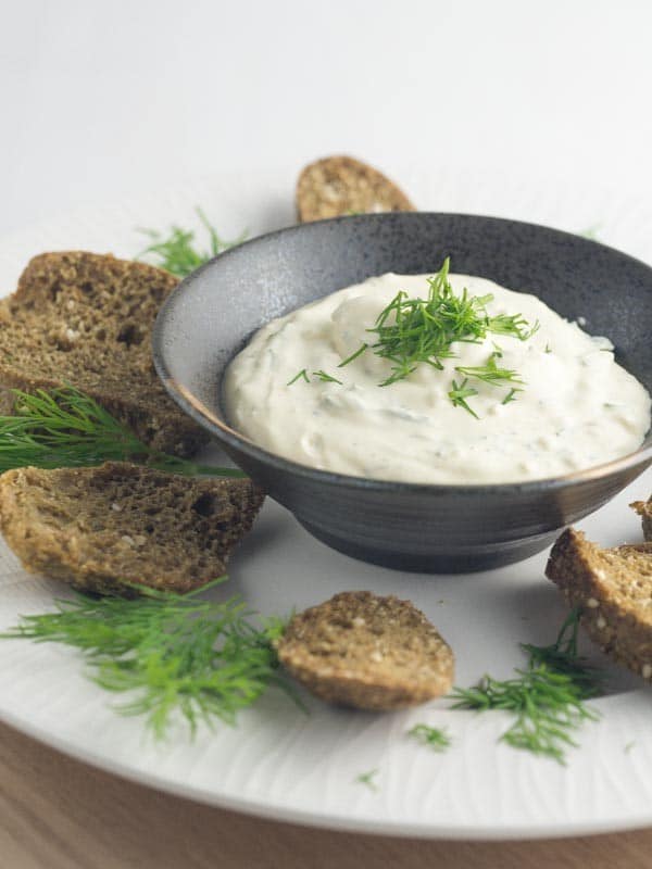 bowl of creamy dill dip on a plate with keto bread and fresh dill