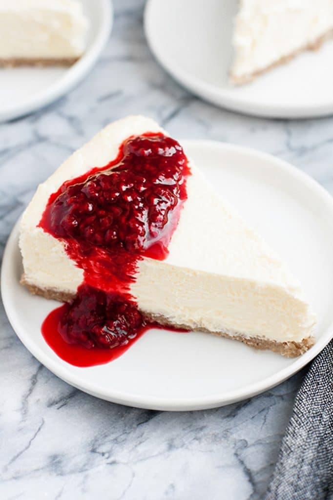 featured image a slice of Nut-Free Keto Cheesecake with raspberry sauce on a small plate atop a marble kitchen counter