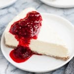 featured image a slice of Nut-Free Keto Cheesecake with raspberry sauce on a small plate atop a marble kitchen counter