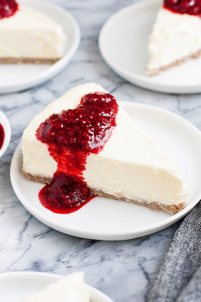 slices of nut-free keto cheesecake drizzled with raspberry sauce served atop small white plates