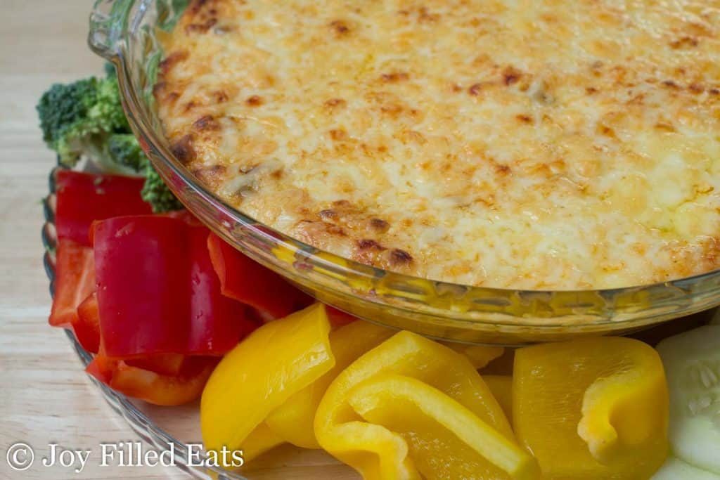 hot cheddar onion dip with bell peppers, sliced cucumbers and broccoli florets on the side