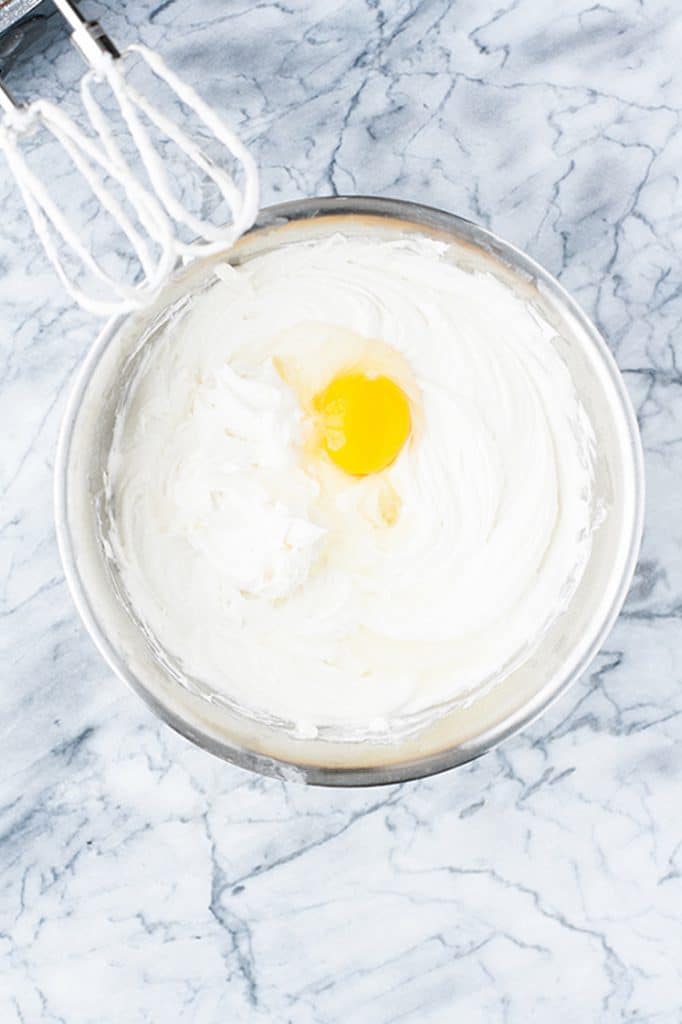 cheesecake batter with an egg whipped in a mixing bowl using an electric mixer