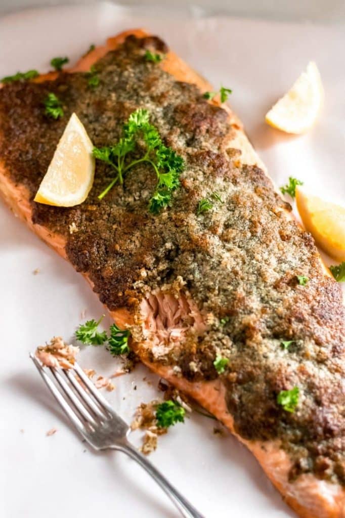 Parmesan crusted salmon with lemon wedges on a baking tray with a fork.